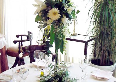 Centro de mesa bajo, blanco. Velas especiales. Longiflorum. Margarita. Orquídea Dendrobium. Crisantemos bola. Verdes, hojas de Aralia. Grass